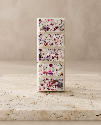 Sofia Dourvari Cherry Amaretto snap bar wax melt with purple and pink confetti inclusions, standing upright on a travertine stone