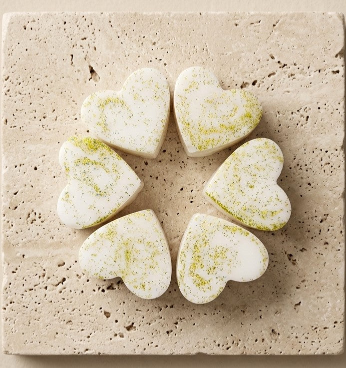 Sofia Dourvari Cardamom & Mimosa heart-shaped coconut wax melts with lime green swirl detailing, arranged in a circle on a travertine tile