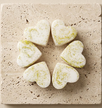 Sofia Dourvari Cardamom & Mimosa heart-shaped coconut wax melts with lime green swirl detailing, arranged in a circle on a travertine tile