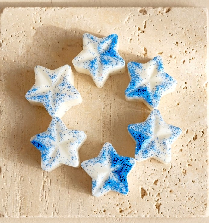 Sofia Dourvari Dove star-shaped coconut wax melts with vivid blue shimmer detailing, arranged in a circle on a pale wooden surface