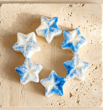 Sofia Dourvari Dove star-shaped coconut wax melts with vivid blue shimmer detailing, arranged in a circle on a pale wooden surface