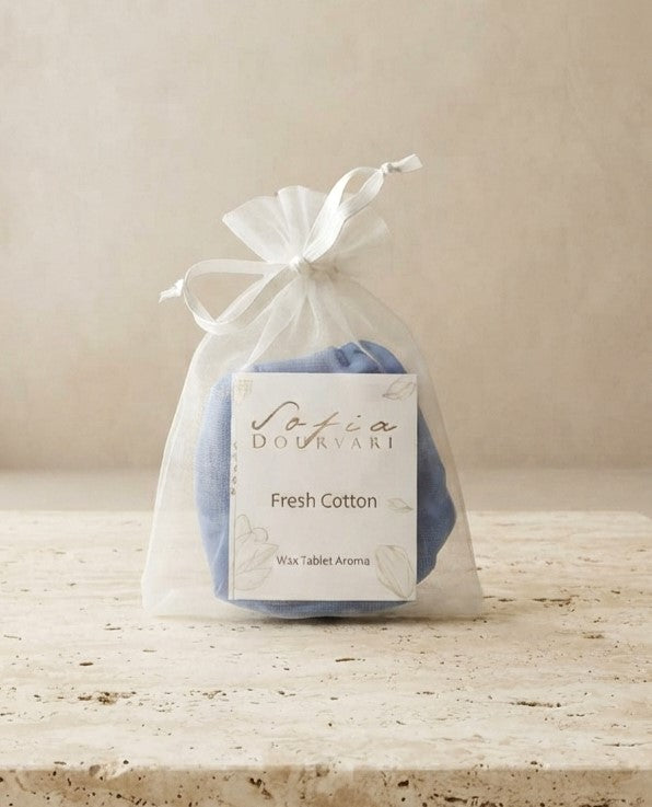 Sofia Dourvari Fresh Cotton Wax Tablet Aroma in a tied white organza bag with branded label, blue wax tablets visible inside, on a travertine stone surface