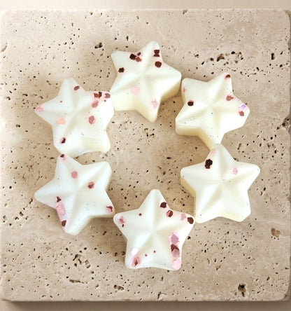 Sofia Dourvari Musk star-shaped coconut wax melts with delicate rose gold flake detailing, arranged in a circle on a travertine tile