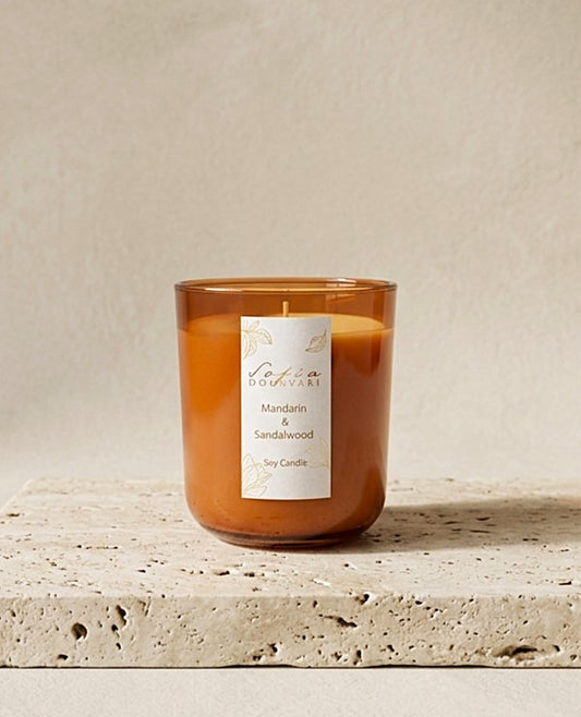 Sofia Dourvari Mandarin & Sandalwood soy scented candle in a warm amber glass vessel, on a travertine stone surface