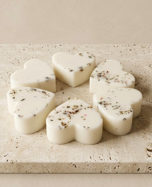 Sofia Dourvari Mandarin & Sandalwood heart-shaped coconut wax melts with dried herb flecks, arranged in a circle on a travertine stone tile