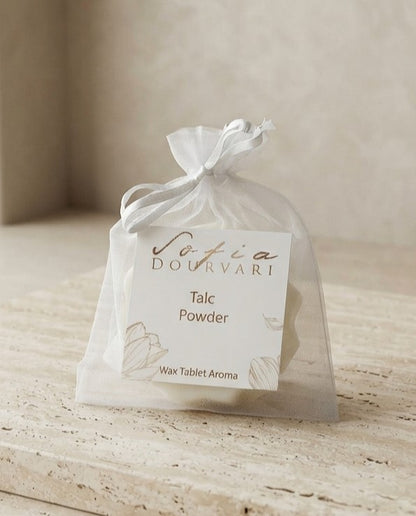 Sofia Dourvari Talc Powder Wax Tablet Aroma in a tied white organza bag with gold-script branded label, on a pale wooden surface