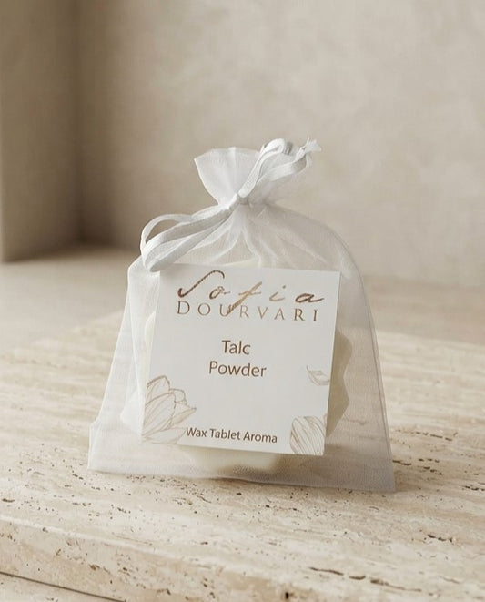 Sofia Dourvari Talc Powder Wax Tablet Aroma in a tied white organza bag with gold-script branded label, on a pale wooden surface