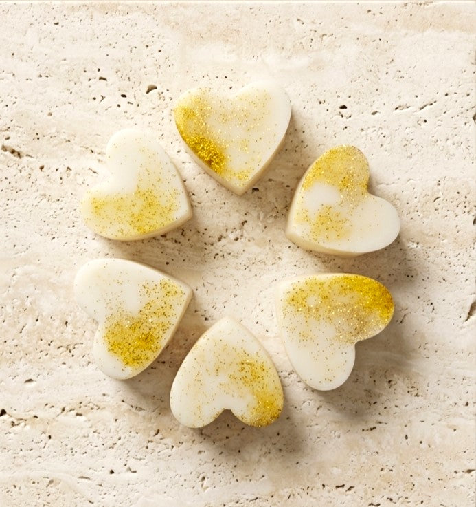 Sofia Dourvari Madagascan Vanilla heart-shaped coconut wax melts with gold shimmer detailing, arranged in a circle on a travertine stone surface